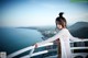 A woman in a white dress standing on a balcony overlooking the ocean.