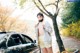 A woman standing next to a black car on a road.