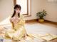 A woman in a yellow kimono sitting on a white rug.