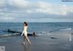 A woman in a white dress walking on the beach.